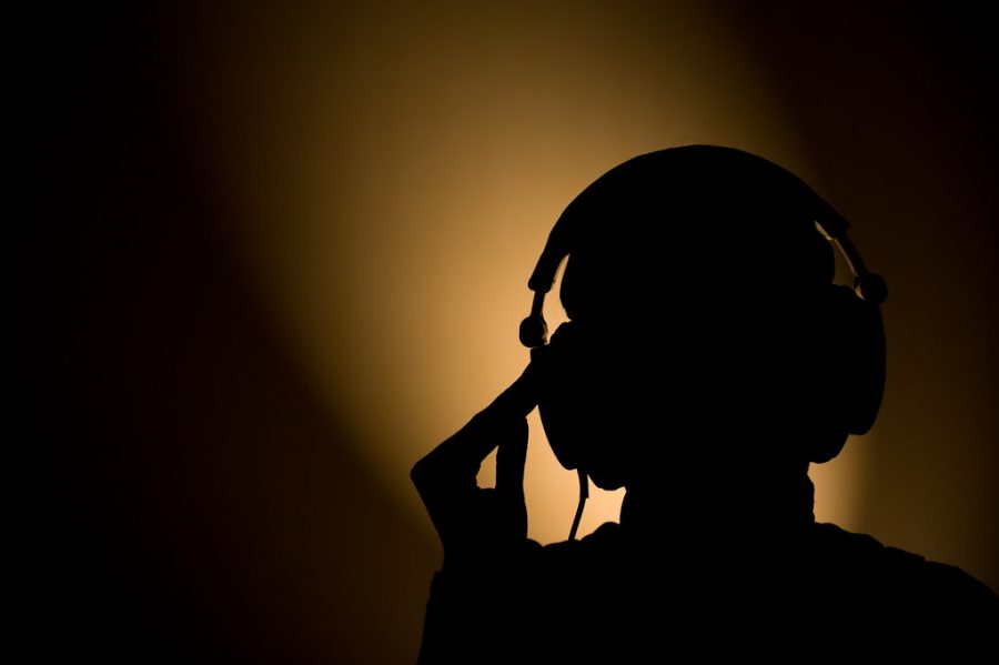 A silhouette slides headphones on by computer light. 