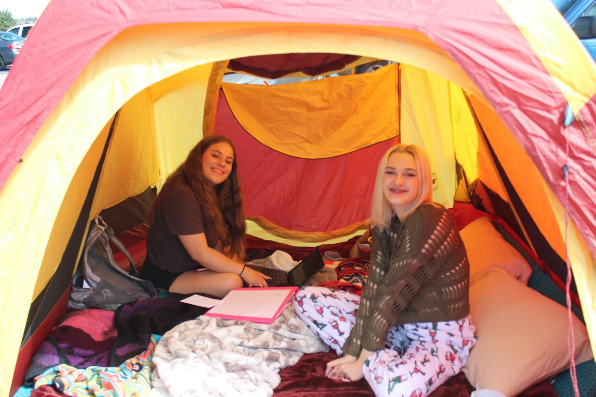 Two seniors hanging out inside of a tent  in the parking lot as part of a senior prank.