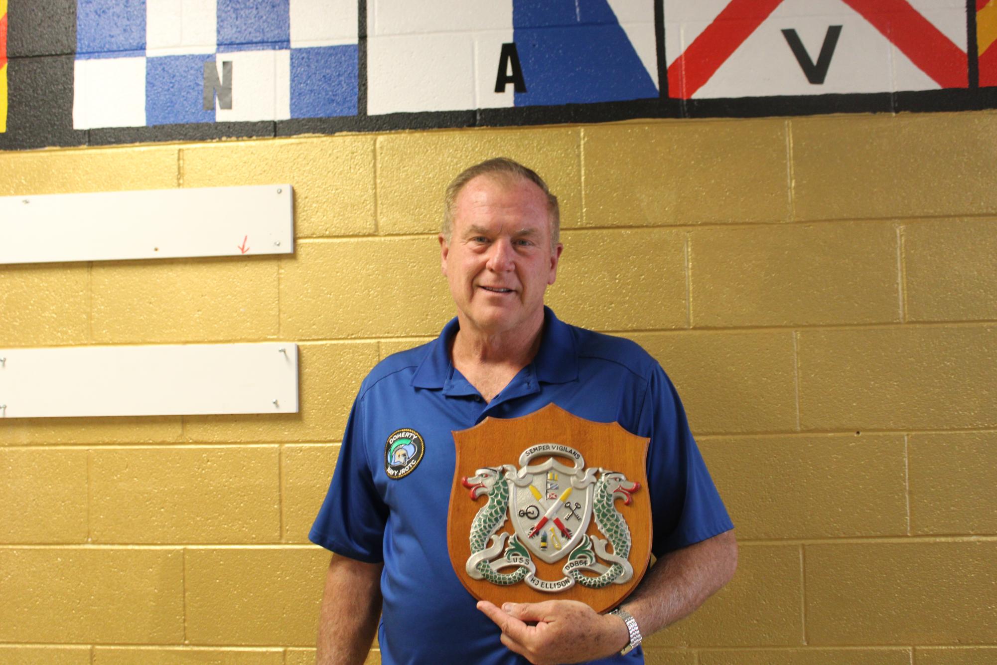 Captain Craig Thomas holding his favorite and most colorful plague In front of the plaque wall in the hall of honor.