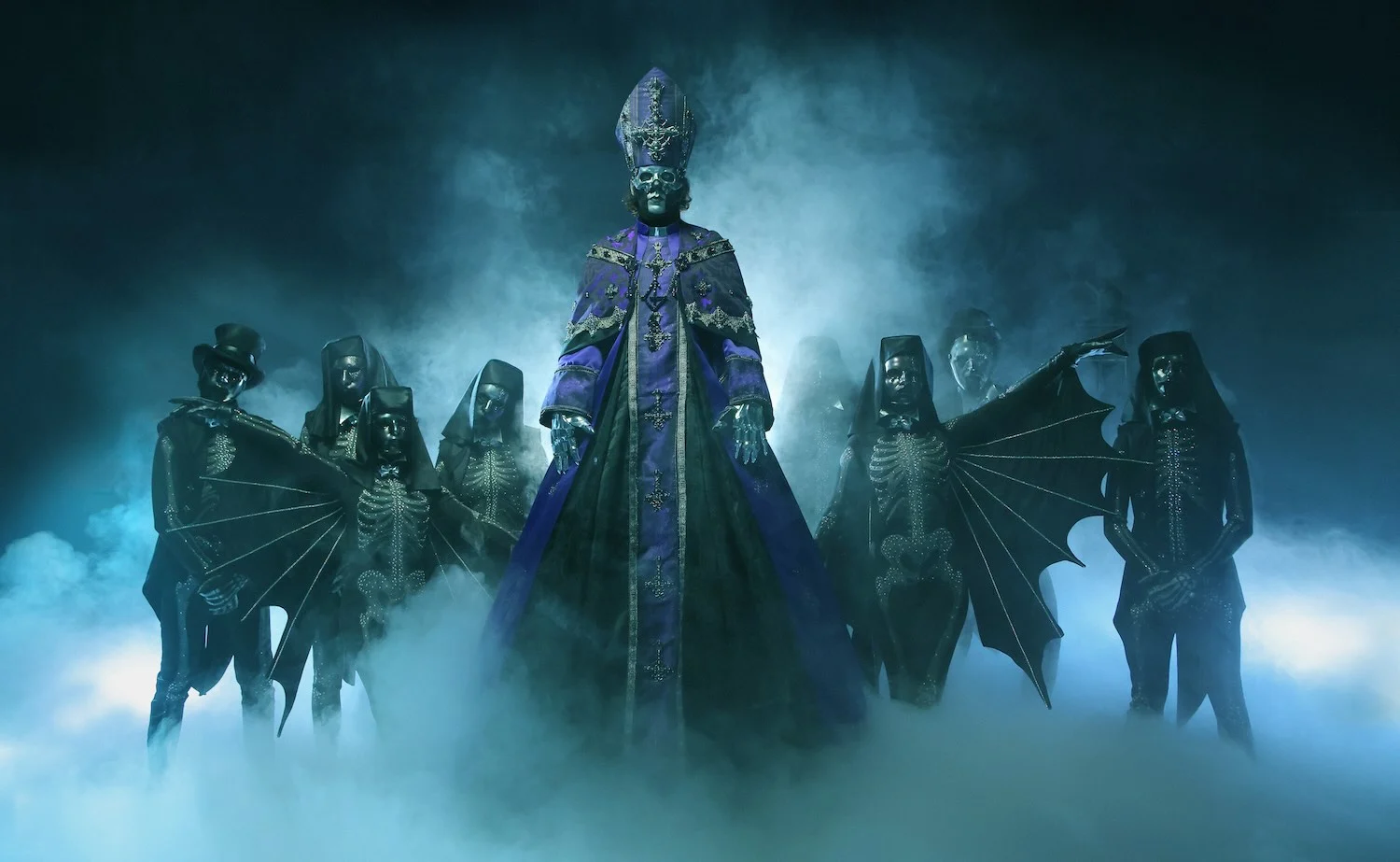 A man in a pope costume surrounded by people dressed in black skeleton jumpsuits.